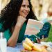 Smiling woman reading a book at a picnic in a sunny park setting.